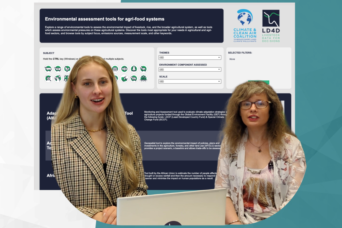 Two women sit at a laptop in front of a backdrop of a data dashboard