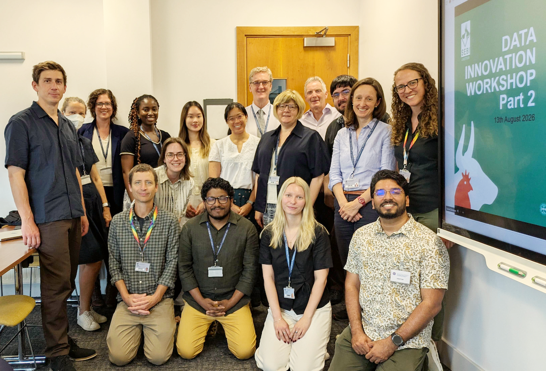 A group of people pose of mixed genders and ethnicities pose for a picture in a meeting room.